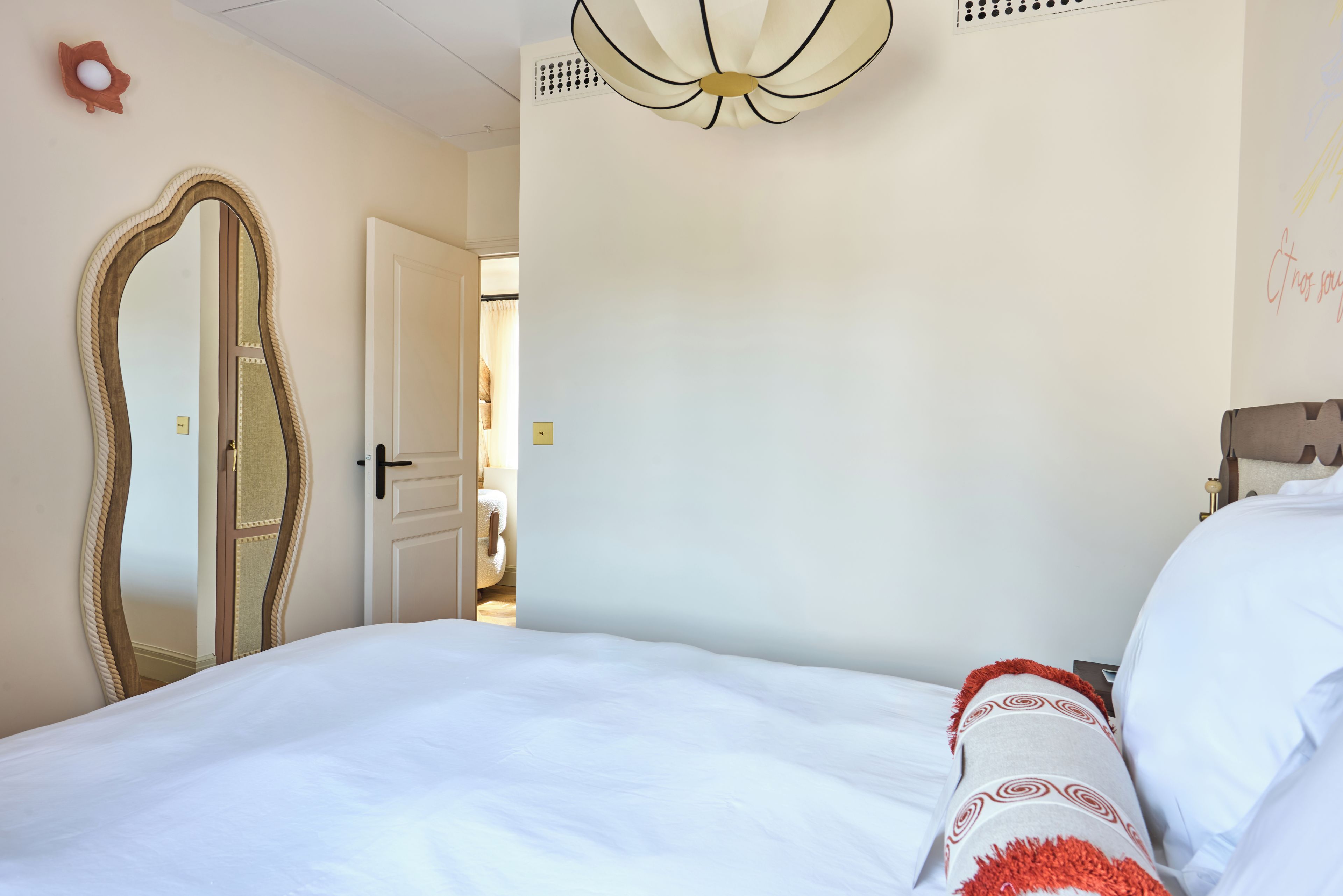Une chambre à coucher avec un grand lit, un miroir, une porte et un luminaire au plafond.