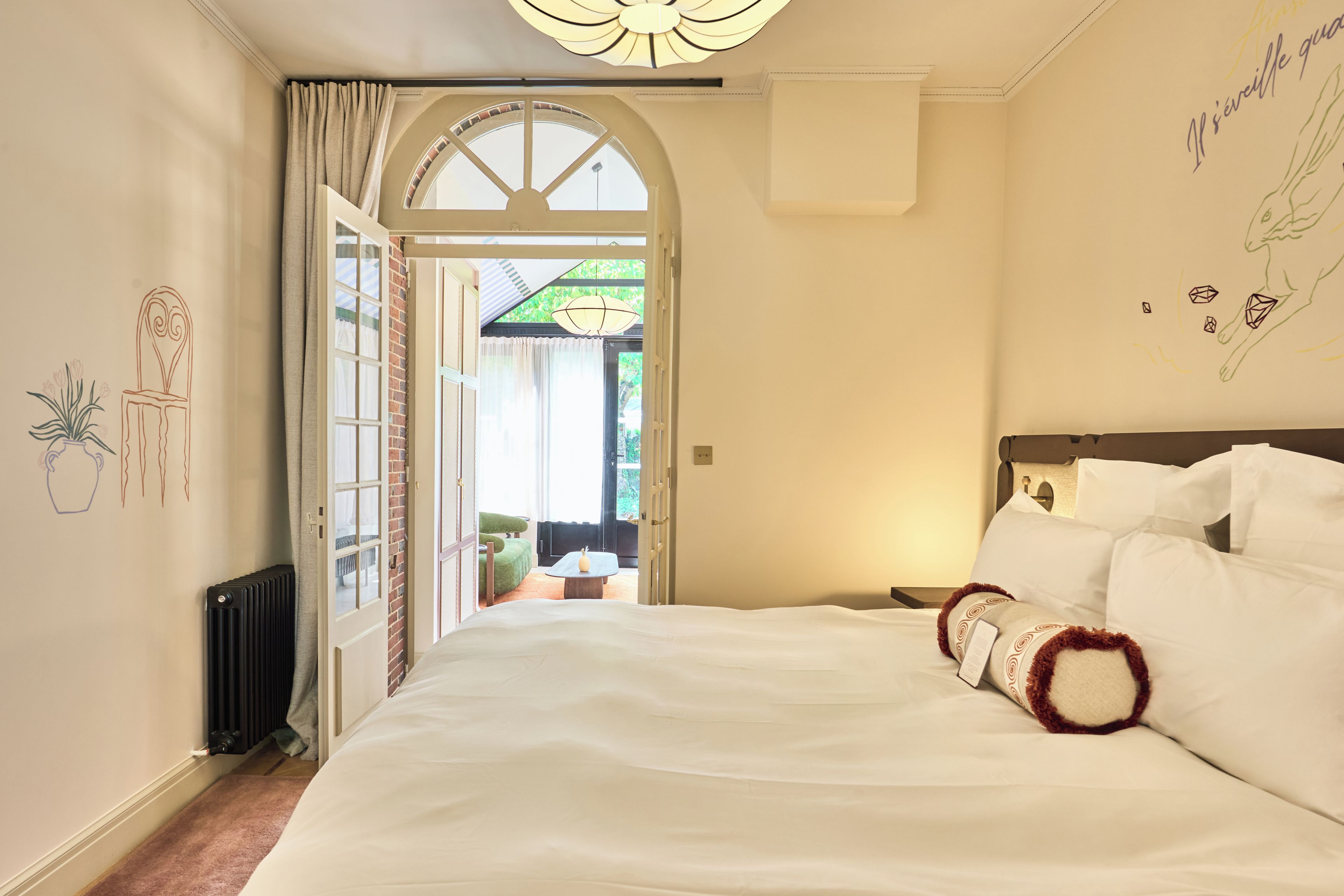 A hotel room with a large bed, a view through an open door, and a ceiling fan.