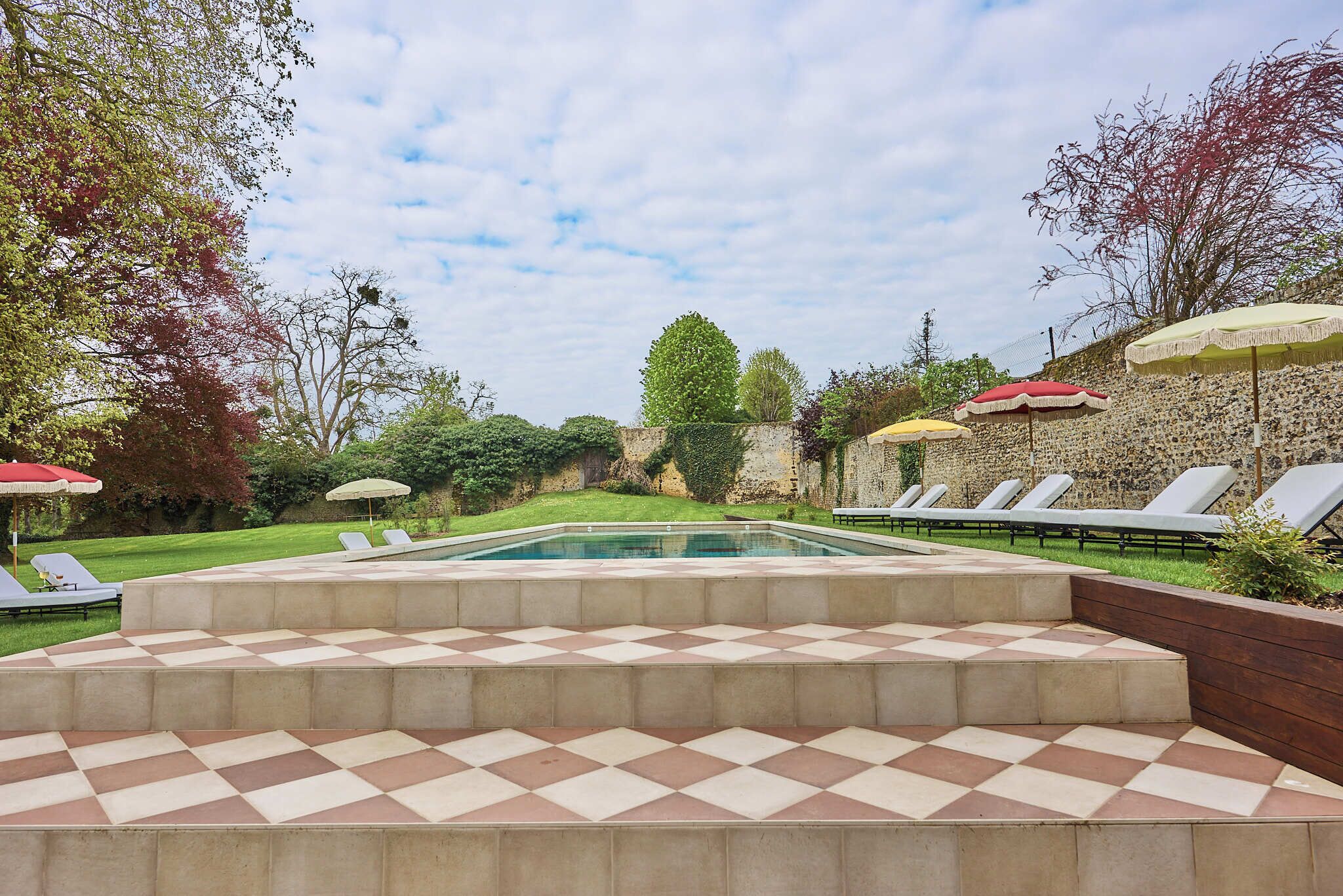 Un espace piscine doté d’un sol à carreaux, de chaises longues et de parasols.