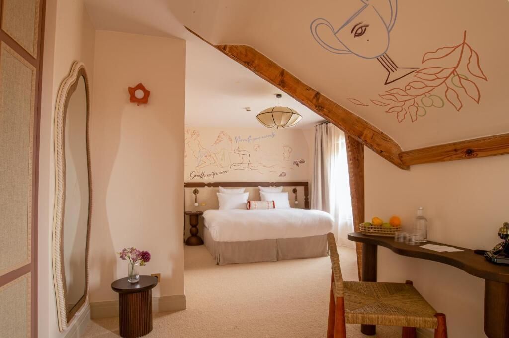 A bedroom with a bed, a bedside table with fruit, a chair, and a wall with a drawing.