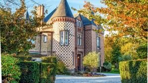 Un edificio histórico con una torre, fachada a cuadros y un jardín bien cuidado.
