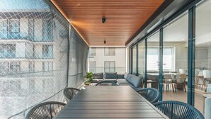 Een modern terras met een lange tafel en rieten stoelen, met uitzicht op een stadslandschap.