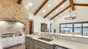 A kitchen with a stone wall, wooden beams, a large island with a sink, and a view of a lake.