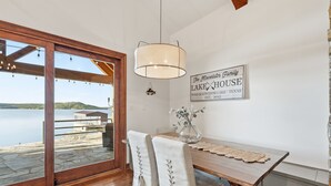 A dining area with a wooden table, chairs, a hanging light fixture, and a view of a lake.