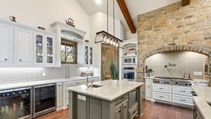 A kitchen with a large island, built-in ovens, and a stone fireplace.