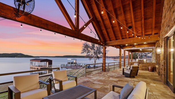 A covered outdoor seating area with stone flooring, wooden beams, and string lights.