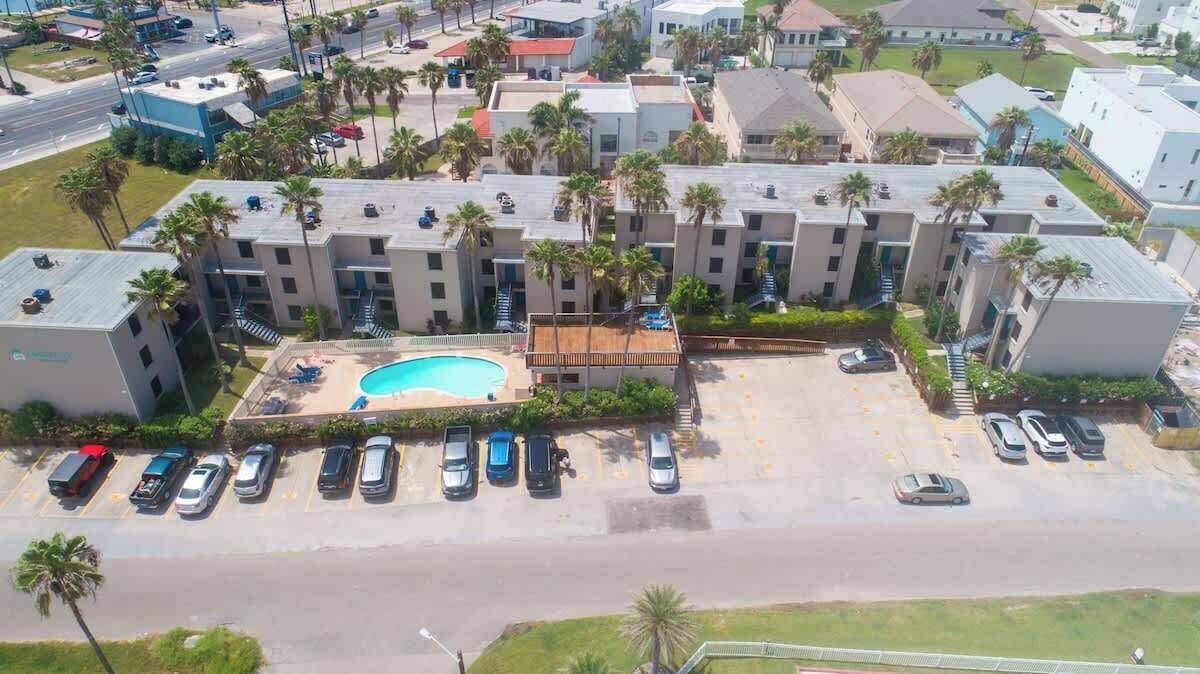 Vista aérea de un hotel con piscina, varios espacios de estacionamiento y una hilera de palmeras.