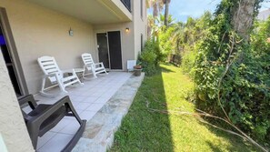 A patio with outdoor seating, a door, and a small garden area with grass and plants. - Island Condo - 1st Floor - Pool - Patio (South Padre Island)