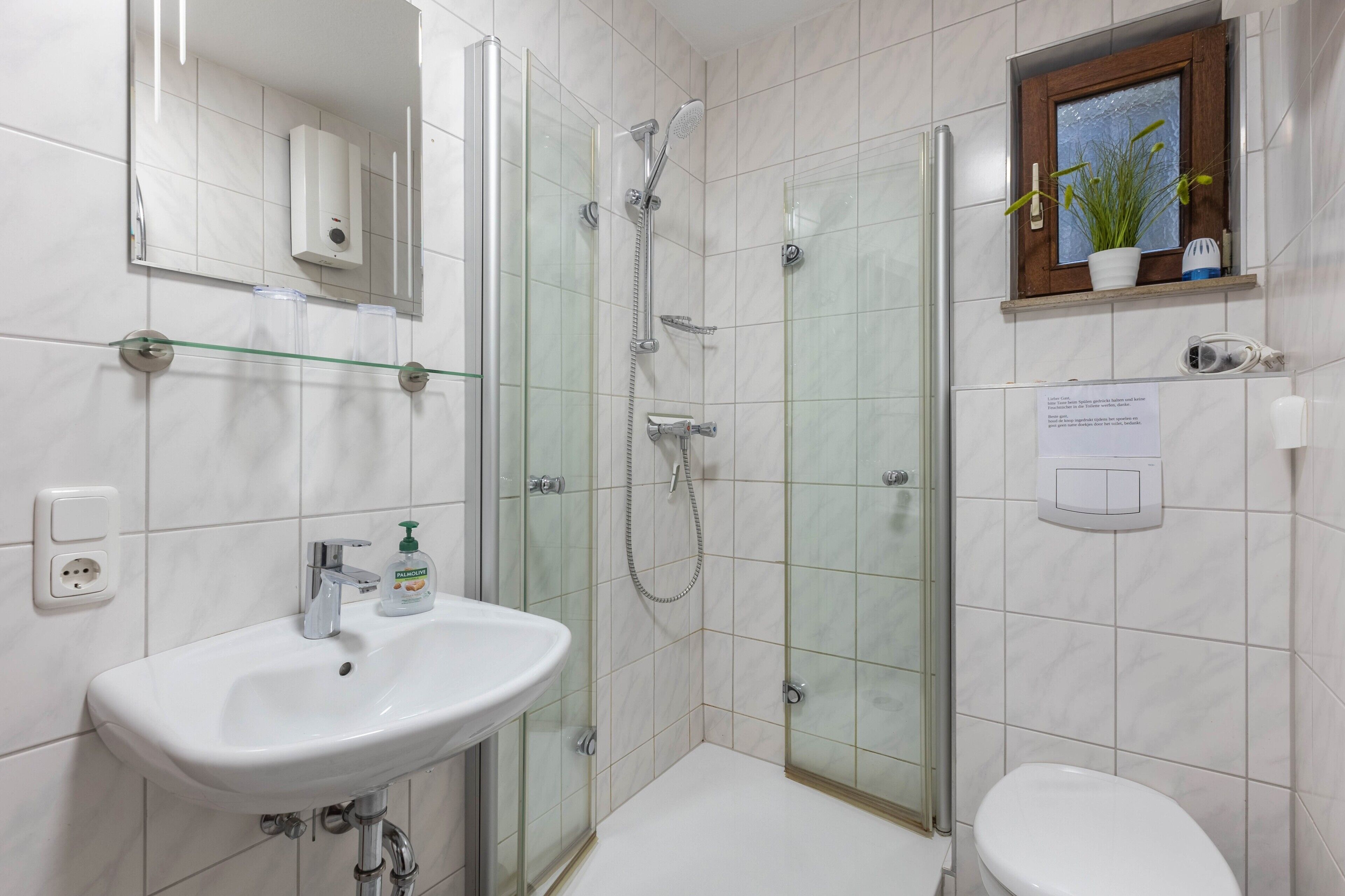 A modern bathroom with a glass-enclosed shower, a white sink with a soap dispenser, and a toilet.