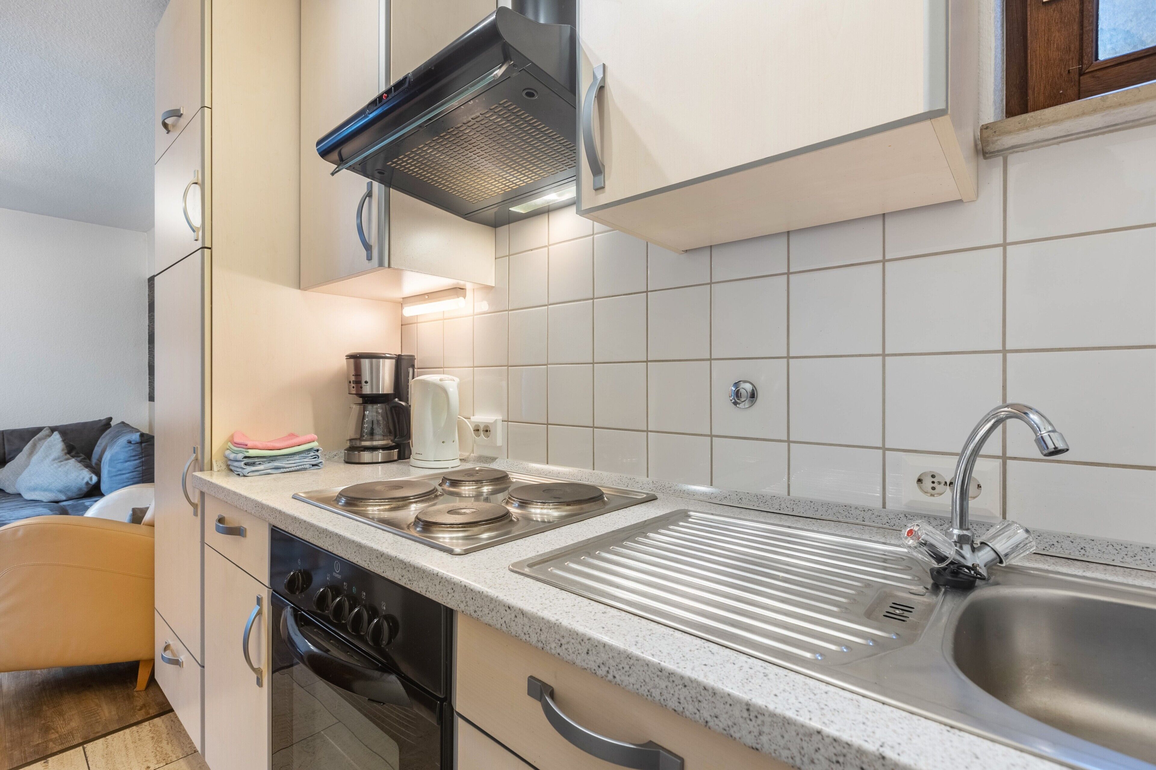 A compact kitchen with a stove, sink, and oven, a small coffee maker, and a window above the sink.