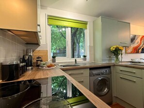 Eine moderne Küche mit integriertem Wasch- und Trockner, einem großen Fenster mit Blick auf Bäume und einer Holzarbeitsplatte.