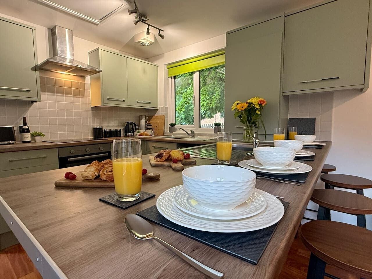 The breakfast bar serves as a place to eat together as a group, here set with white bowls, orange juice, and food on wooden boards.