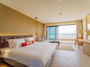 Une chambre d’hôtel avec un grand lit, un bureau, une chaise et une vue sur la mer.