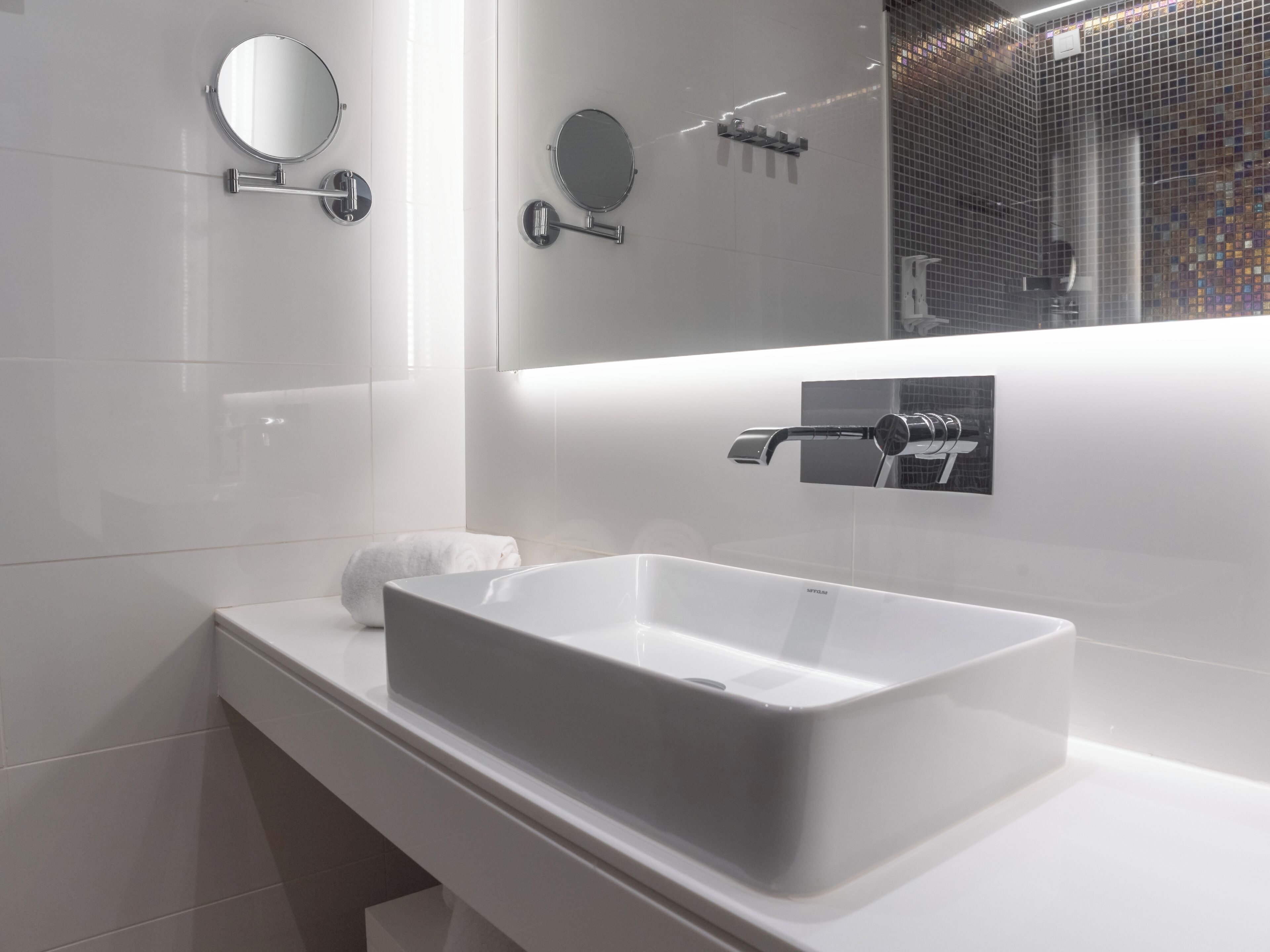 Een moderne badkamer met een rechthoekig wastafel, een ronde spiegel en een handdouche.