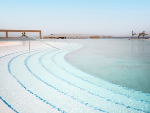 A clear pool with blue lines, a wooden deck, and a distant building. - Royal Horizon Beijo Mansão - Ponta Sino (Santa Maria)