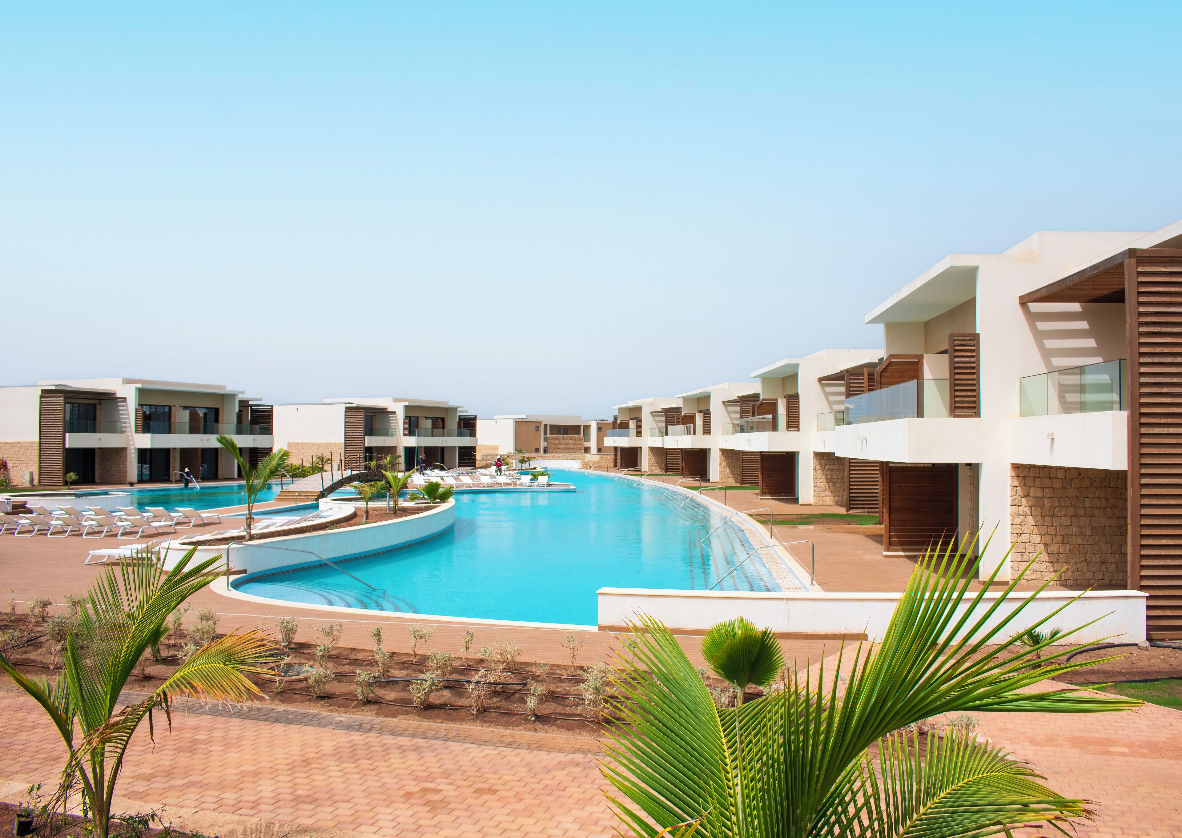 Ein modernes Resort mit einem zentralen Schwimmbad, mehreren Balkonen und einem Pflasterweg.