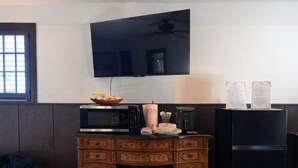 Eine kompakte Küche mit Mikrowelle, Kaffeemaschine und Kühlschrank. Ein Fernseher ist an der Wand oberhalb der Arbeitsfläche angebracht.