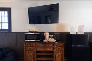 Eine kompakte Küche mit Mikrowelle, Kaffeemaschine und Kühlschrank. Ein Fernseher ist an der Wand oberhalb der Arbeitsfläche angebracht.