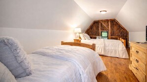 Ein Schlafzimmer mit zwei Betten, Holz-Kopfteilen, einer Holzkommode und einer geneigten Decke.