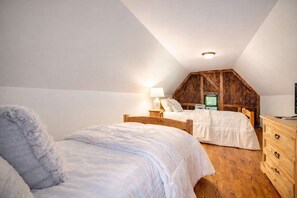 Ein Schlafzimmer mit zwei Betten, Holz-Kopfteilen, einer Holzkommode und einer geneigten Decke.