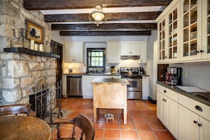 A kitchen with white cabinets, a wooden island, a stone wall, and a tiled floor. - Storybook 3-Cottage Mountain Getaway (Banner Elk)