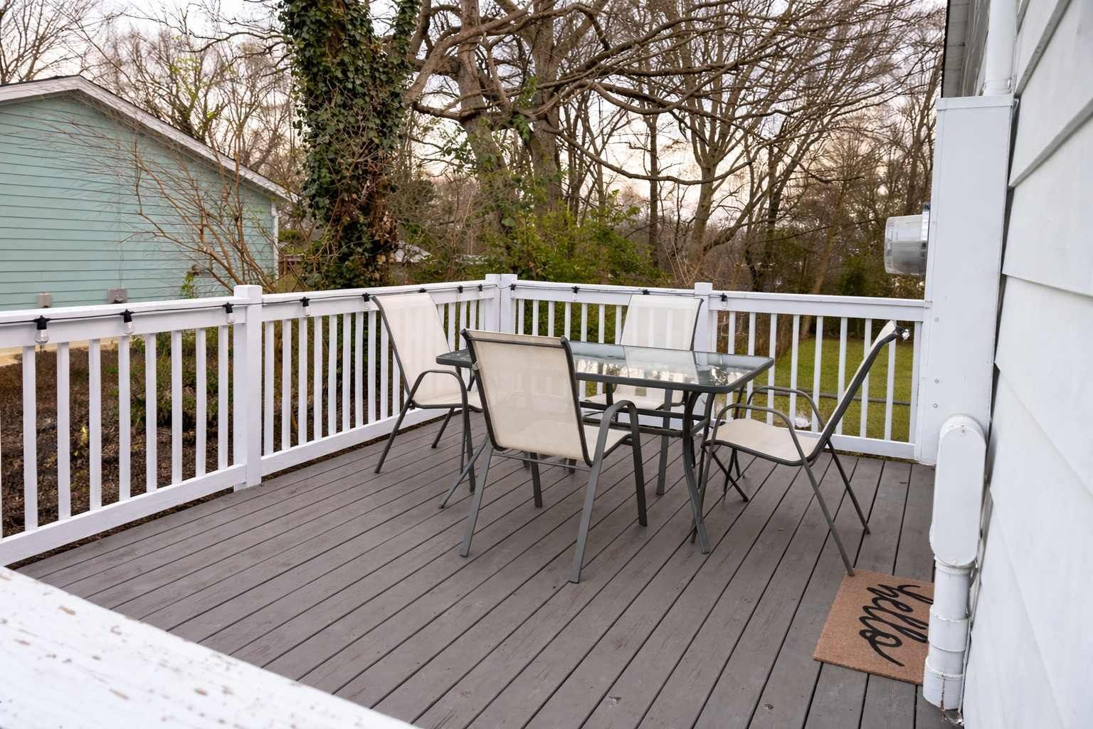 A covered outdoor deck with a table and chairs, surrounded by a white railing.