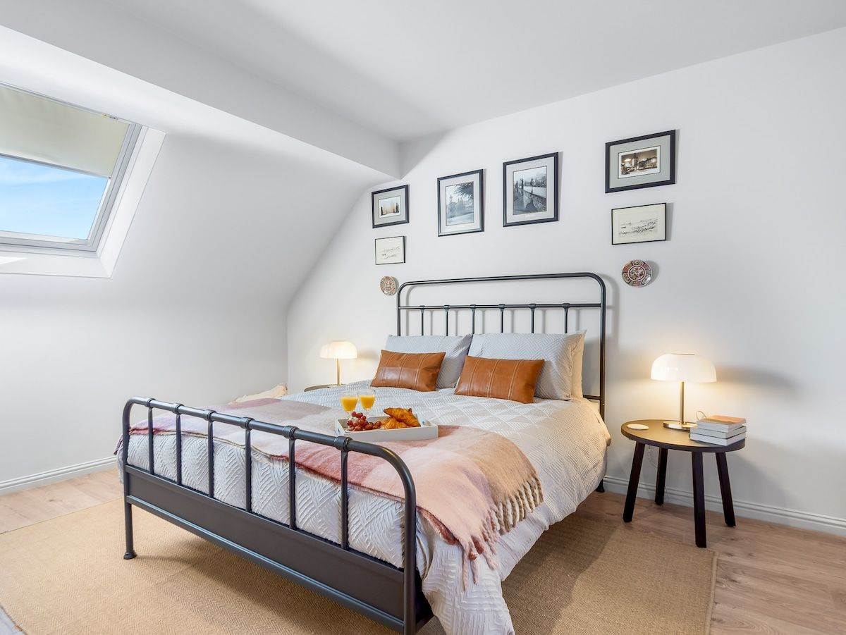 Une chambre à coucher avec un lit, des tables de chevet, une fenêtre et des tableaux accrochés au mur.