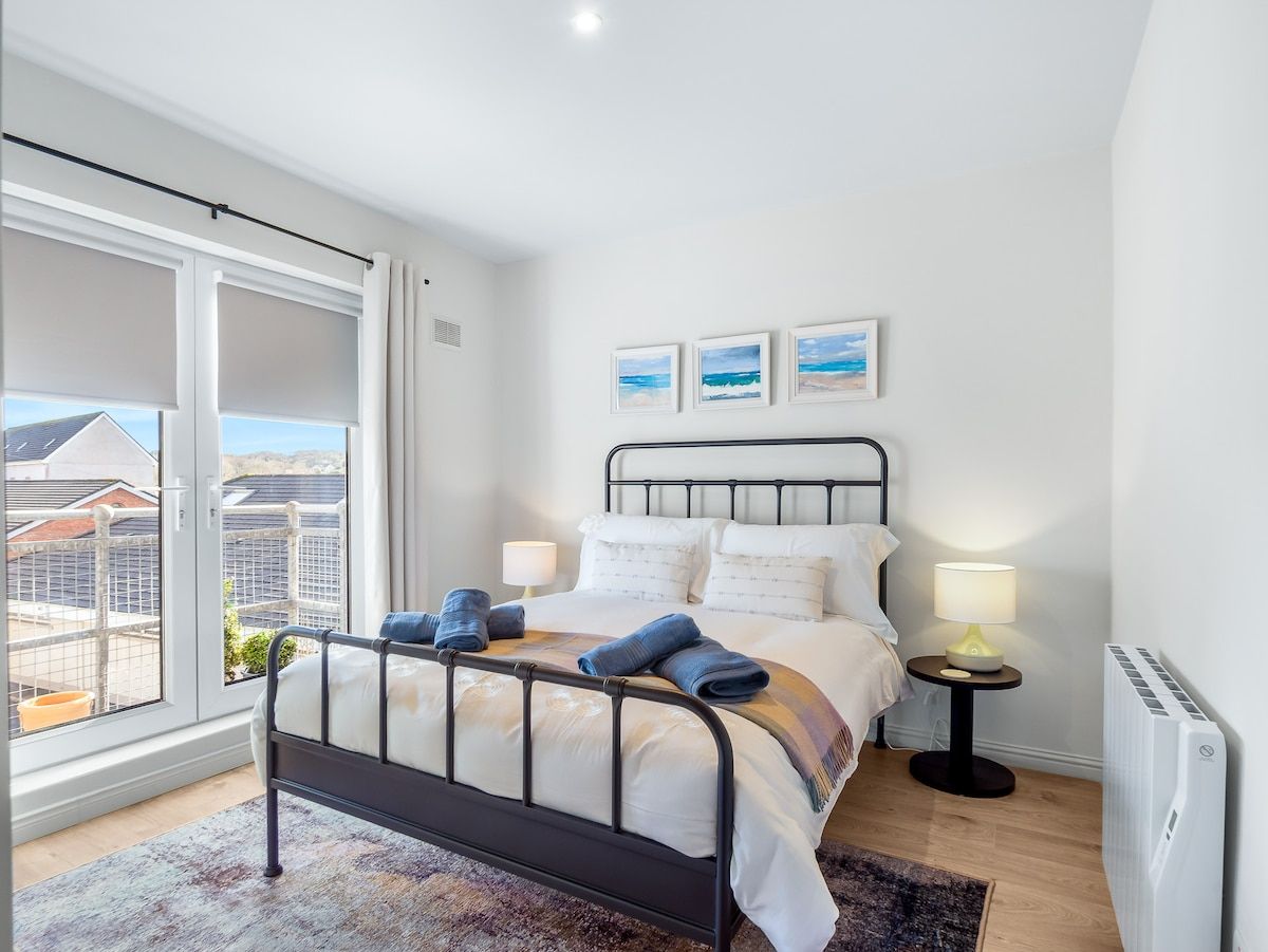 Une chambre à coucher avec un lit, des tables de chevet, un radiateur et une vue sur l’extérieur.