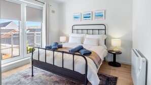 Een slaapkamer met een bed, twee nachtkastjes, een radiator en een raam met uitzicht op gebouwen.
