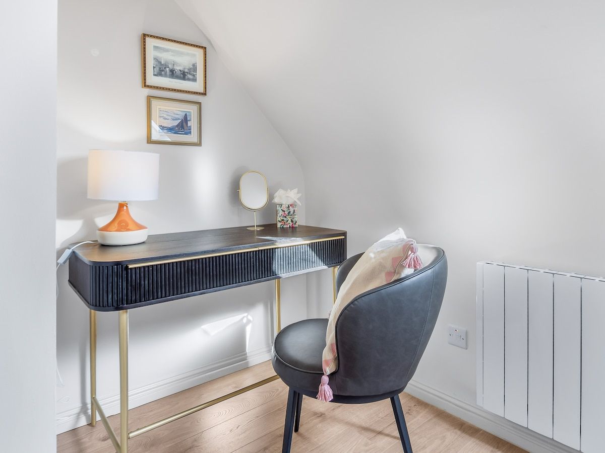 Une chambre moderne équipée d’un bureau, d’une chaise, d’une lampe et de tableaux encadrés accrochés au mur.