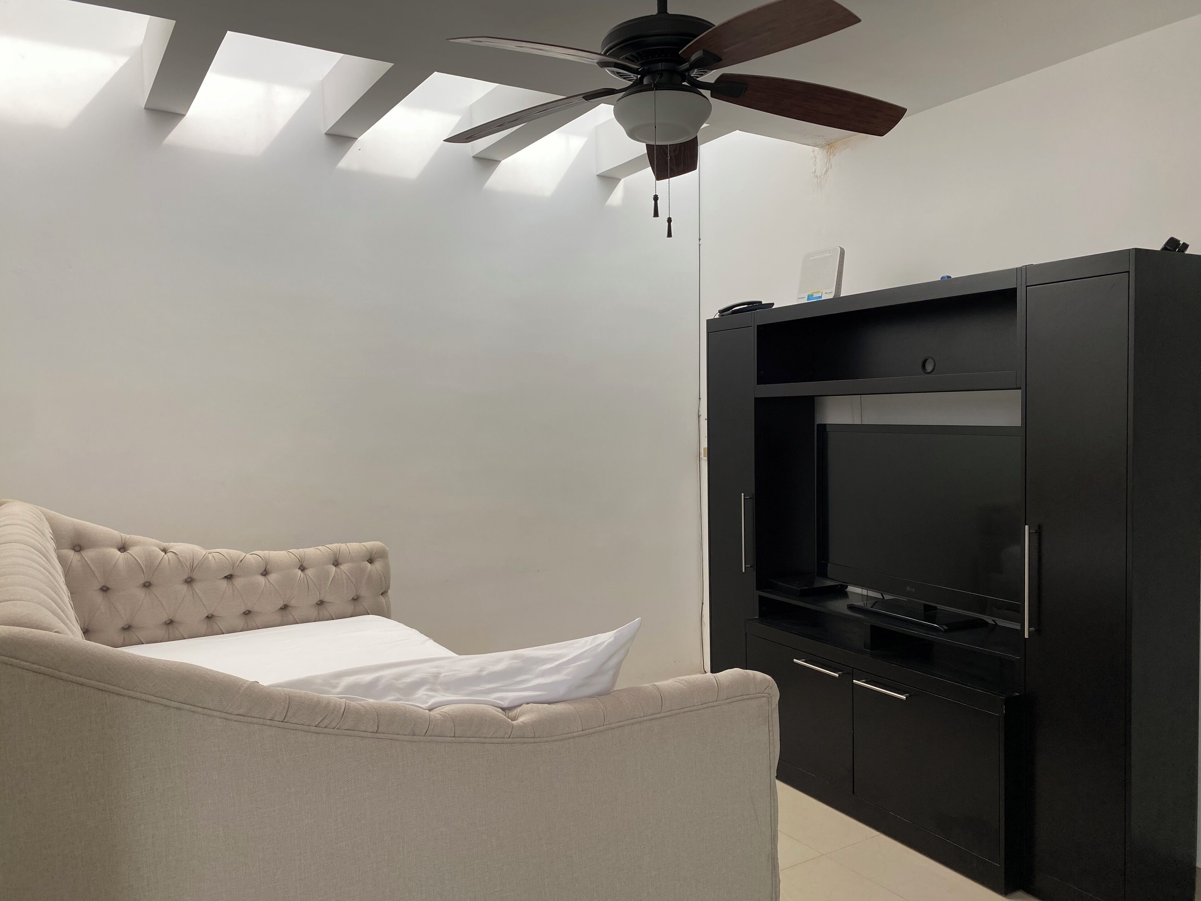 Une chambre avec un lit, un ventilateur de plafond et un meuble noir pour le matériel de divertissement.