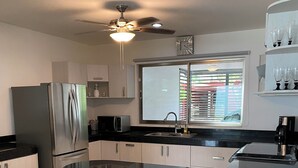 A modern kitchen with a stainless steel refrigerator, a microwave, a sink, and a window with blinds. There are three bar stools with metal bases. - Beautiful comfortable home with swimming pool (Mérida)
