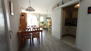 Uma área de refeições com mesa e cadeiras de madeira, um lustre pendurado e uma cozinha com armários e eletrodomésticos.