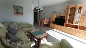 Uma sala de estar com um sofá verde, um armário de madeira, uma mesa de jantar com cadeiras e uma televisão.
