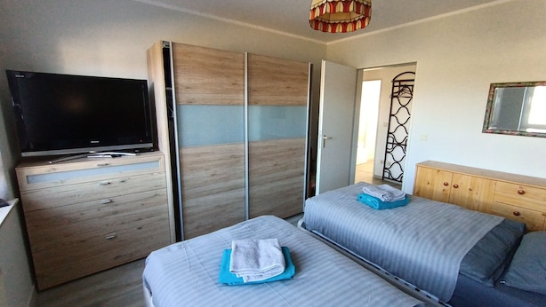 Quarto com televisão, duas camas, guarda-roupa e um espelho decorativo.