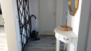 Um corredor com uma porta branca, um aparador branco com uma cesta trançada, um espelho decorativo e um lustre pendurado.