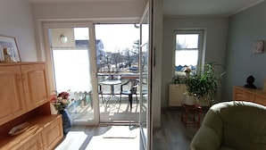 Quarto com porta de vidro deslizante que dá para um alpendre ao ar livre com mesa, cadeiras, planta em vaso e um armário de madeira.