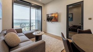 A modern living room with a sofa, round coffee table, and a dining table. There is a large window with a view of the city. - LUMIERE Riverside Signature Residence (Ho Chi Minh City)