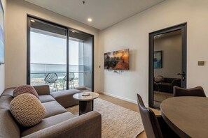 A modern living room with a sofa, round coffee table, and a dining table. There is a large window with a view of the city. - LUMIERE Riverside Signature Residence (An Phu)