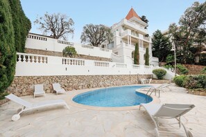 Ein Poolbereich mit Liegestühlen, einer Steinmauer und einem Gebäude mit Balkonen.