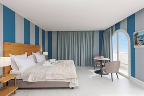 Ein Hotelzimmer mit einem großen Bett, einem Nachttisch, einem Sessel, einem kleinen Tisch und Meerblick.