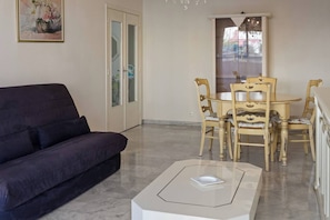 Ein Wohnzimmer mit einem dunkelgrauen Sofa, einem Couchtisch mit Glasplatte und einem Holzes Esstisch mit vier Stühlen.