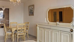 Een eethoek met een ronde tafel en vier stoelen, een wit kastje met een grote spiegel, en een kroonluchter.