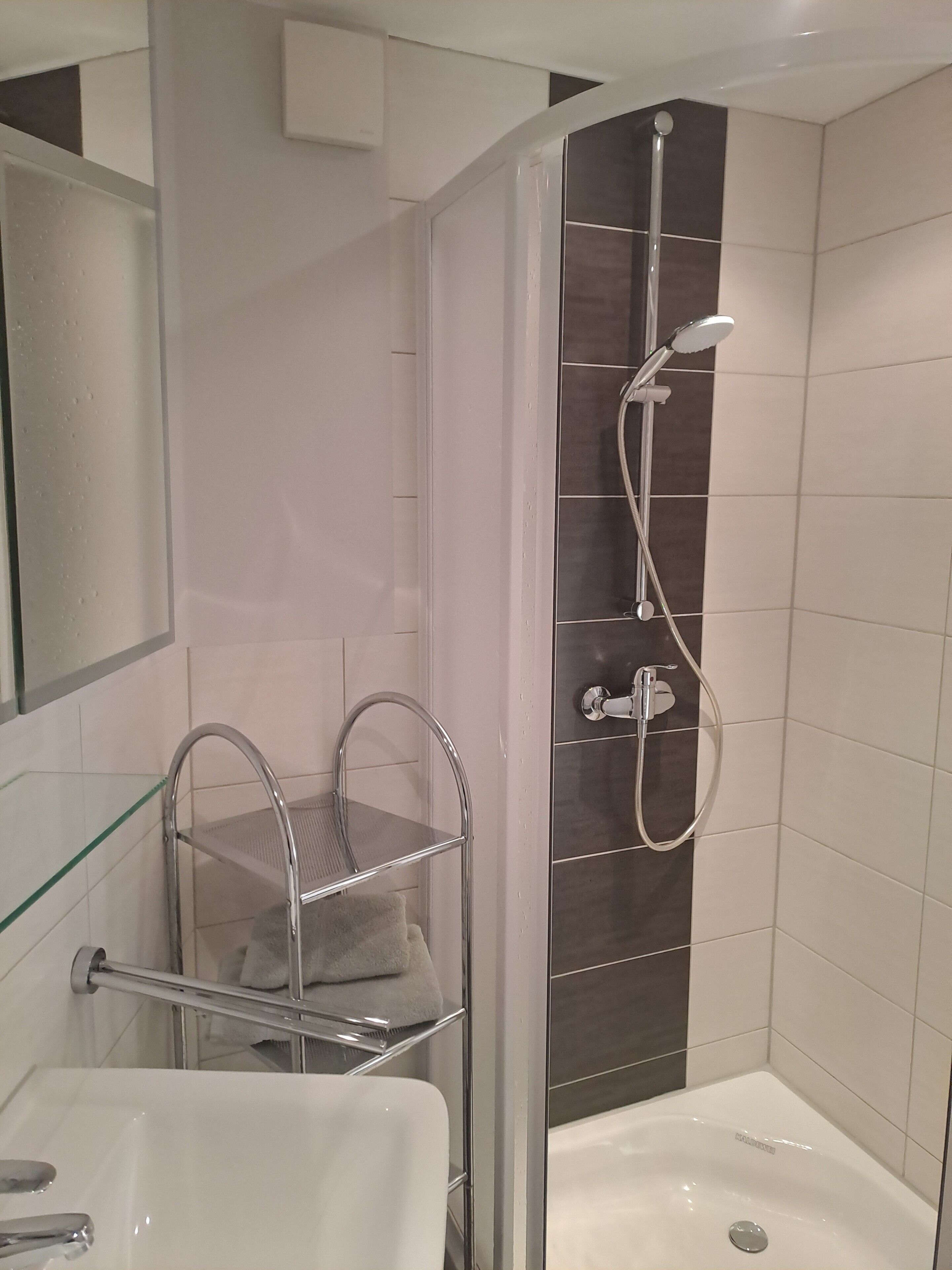 Un baño con ducha, repisa de vidrio y lavamanos.