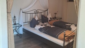 A bed with a canopy, a bedside table, a small table, and a wall-mounted picture.