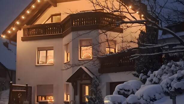 A two-story house with a balcony, a porch, and a snow-covered landscape.