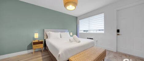 A bedroom with a bed, bedside table, lamp, and a window.