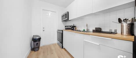 Una cocina compacta con armarios blancos, un microondas, un lavavajillas y una encimera de madera.