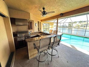 Eine Küche mit einer großen Kochinsel, integriertem Grill und Blick auf einen Swimmingpool.