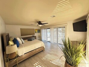 Ein Schlafzimmer mit Bett, Nachttischlampe, Deckenventilator und einem an der Wand montierten Fernseher.